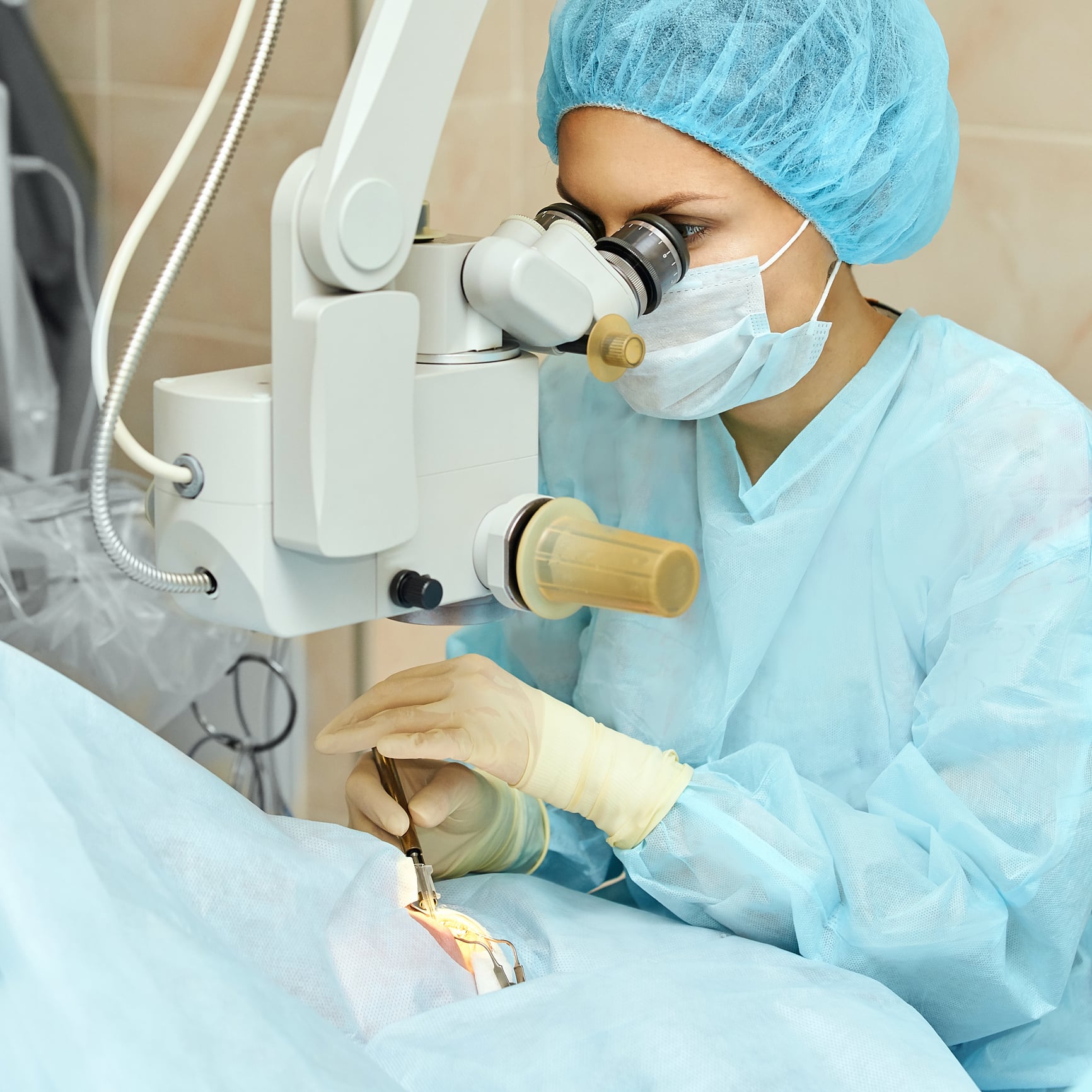 Ophthalmic surgeon in surgical cap and mask operating a femtosecond laser over a patient’s eye